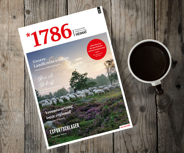 Ein Online Magazin *1786 liegt auf einem rustikalen Holztisch neben einer Tasse Kaffee. Das Titelbild zeigt eine weidende Schafherde in einer malerischen Landschaft mit Bäumen und Feldern.