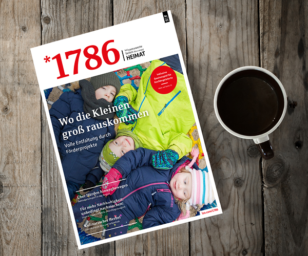 Das Online Magazin *1786 zeigt auf dem Titelbild vier kleine Kinder in Winterkleidung, die auf einer bunten Decke liegen, daneben eine Tasse Kaffee auf einem Holztisch.