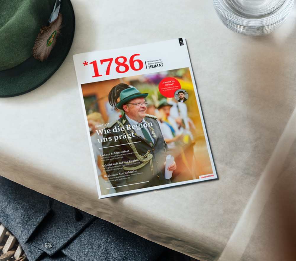 Das Magazin mit dem Titel 1786, auf deren Titelseite ein Mann in traditioneller Schützenfestuniform abgebildet ist, liegt auf einem weißen Tisch neben einem Glas Wasser und einem grünen Schützenfest-Hut mit Feder.