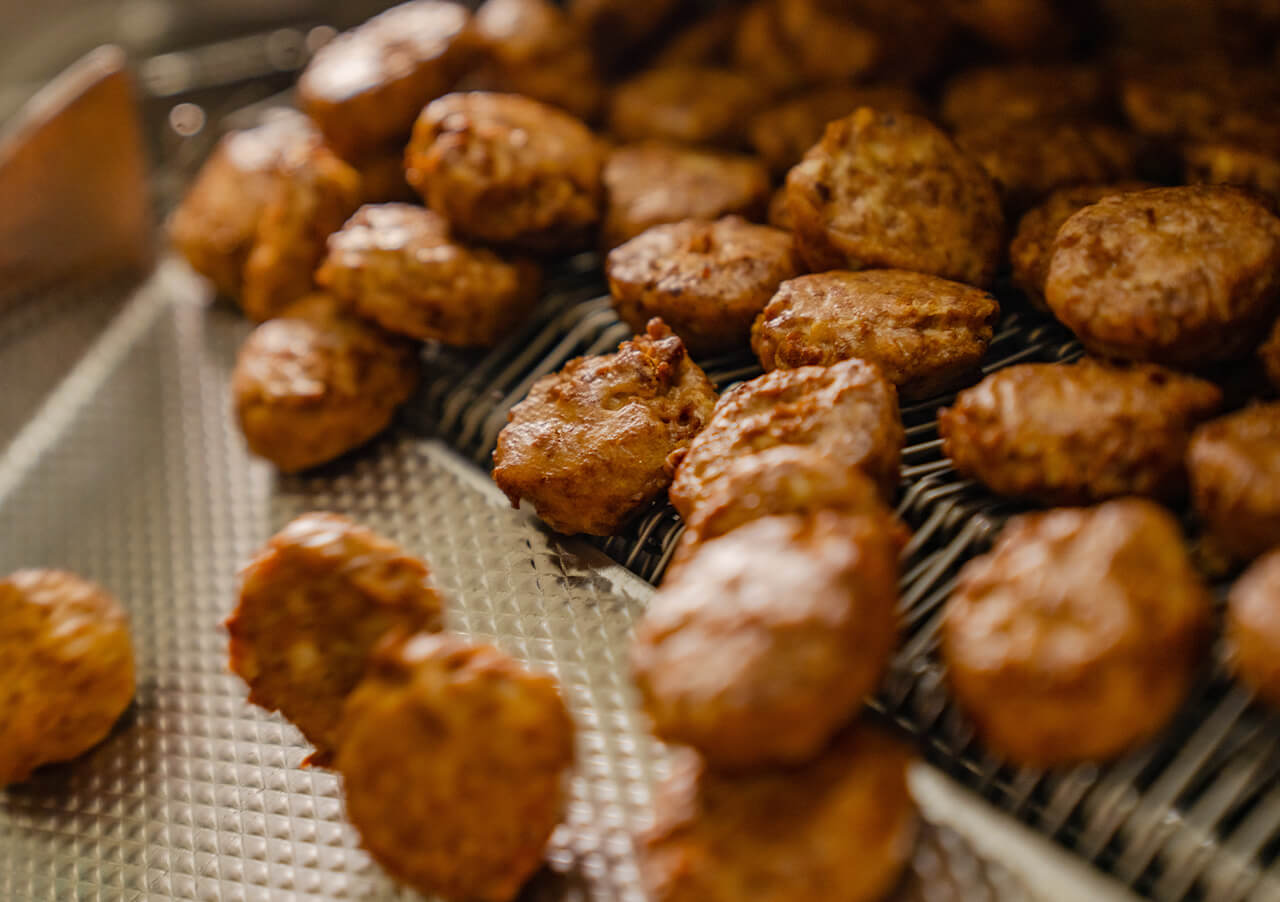 Nahaufnahme von mehreren goldbraunen Hähnchen-Nuggets auf einem Metallförderband in einer Lebensmittelverarbeitungsanlage, die Produktinnovation und Transformation hervorhebt, da die frisch gekochten Nuggets ordentlich in Reihen angeordnet sind.