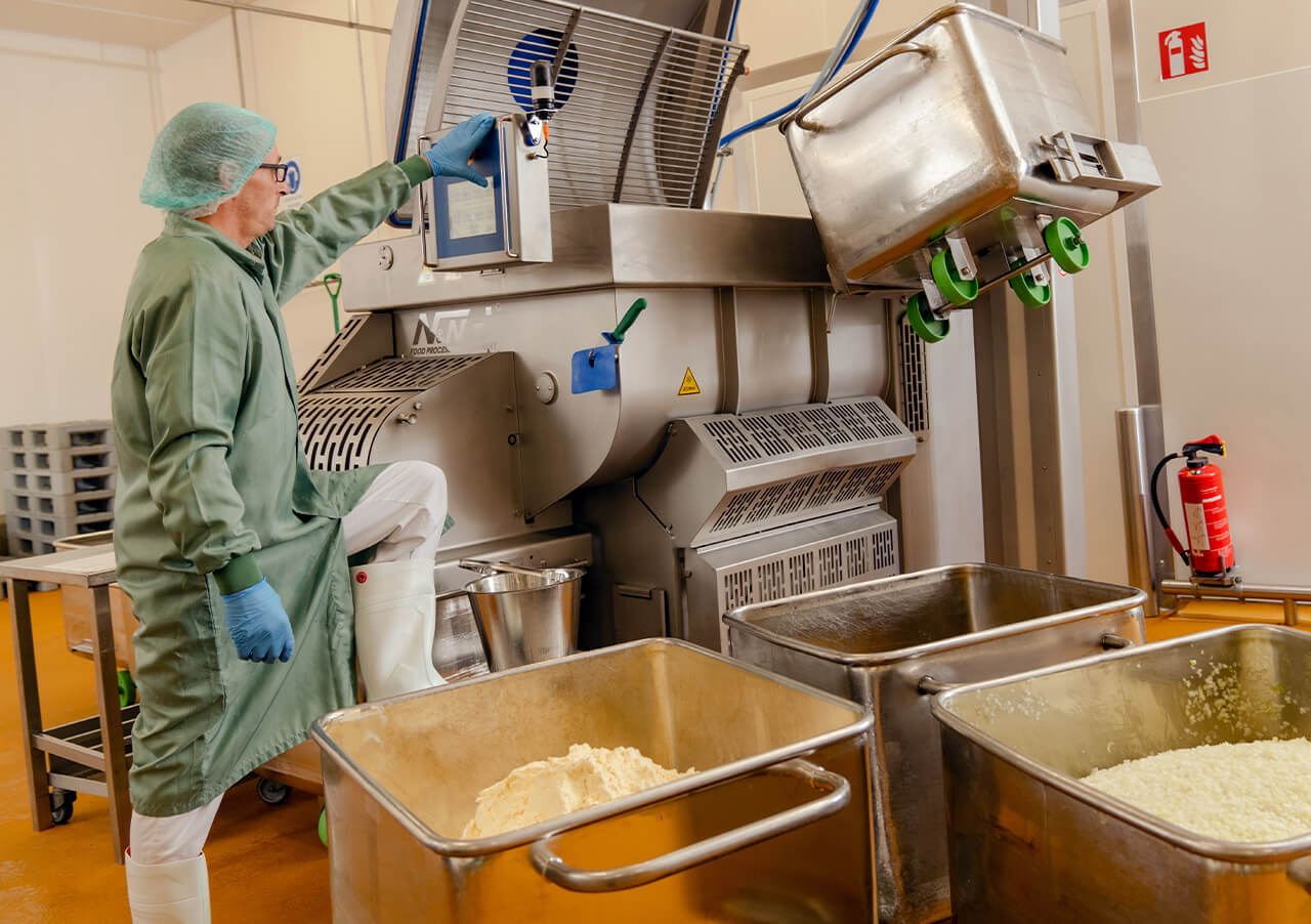 Ein Arbeiter in Schutzkleidung bedient eine industrielle Lebensmittelverarbeitungsanlage - eine Umgebung der Produktinnovation und -transformation - mit großen Metallbehältern, die mit weißen Substanzen gefüllt sind, im Vordergrund und einem Feuerlöscher in der Nähe.