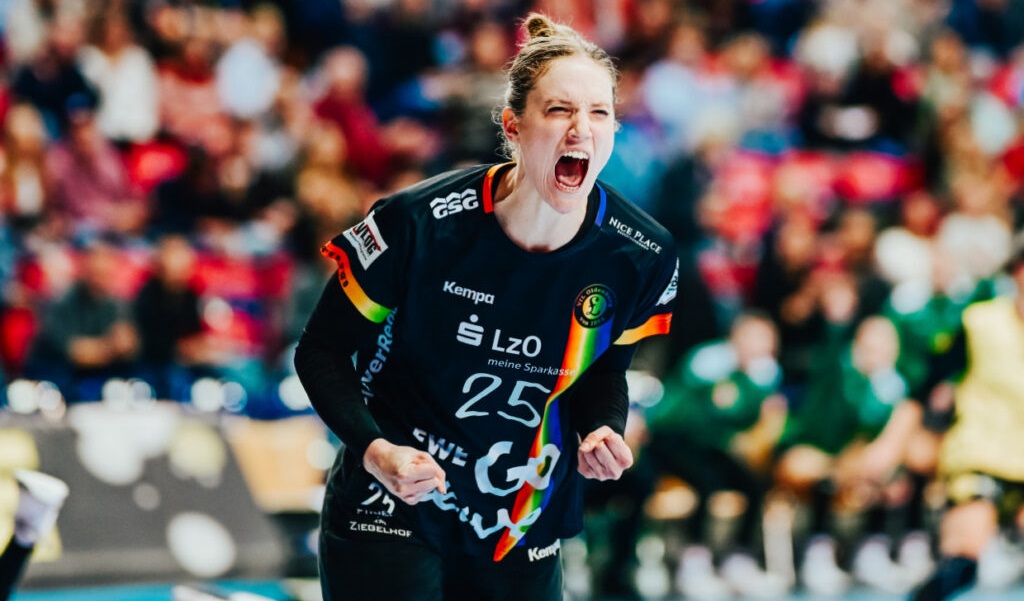 Torhüterin Madita Kohorst, die ein schwarzes Trikot mit der Nummer 25 trägt, feiert leidenschaftlich auf dem Spielfeld, ballt die Fäuste und schreit, während im Hintergrund eine verschwommene Menge zu sehen ist.
