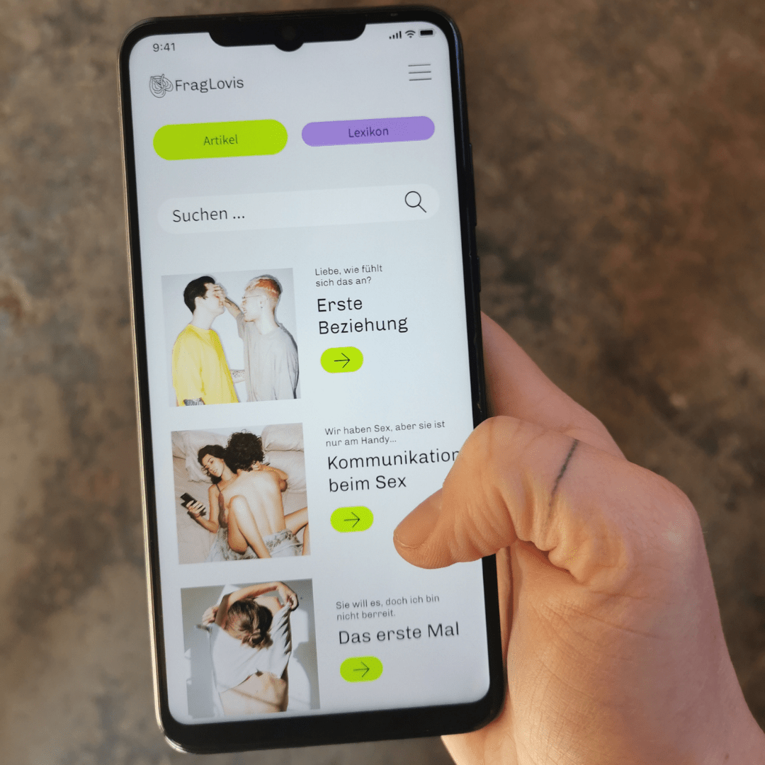 Eine Hand hält ein Smartphone mit dem Display von FragLovis Sexualbildung, das Artikel über Beziehungen und Sex mit ansprechenden Fotos und grünen Pfeilsymbolen für weitere Informationen enthält.