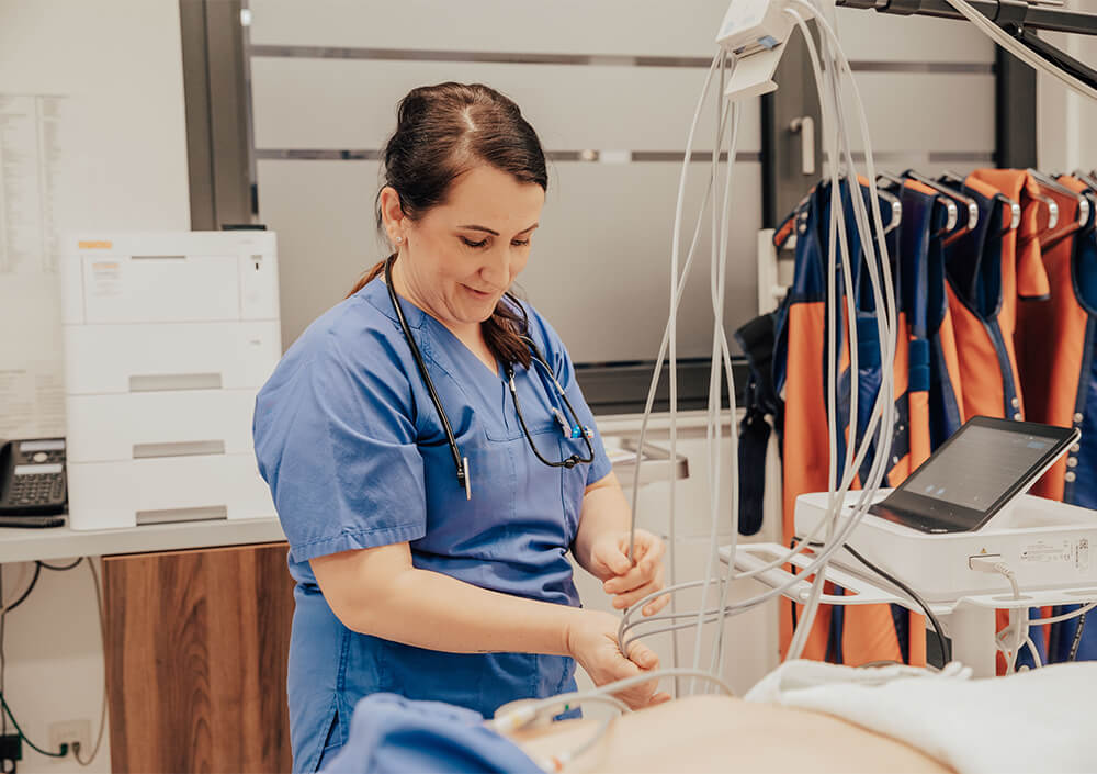 Eine Mitarbeiterin des Gesundheitswesens in blauen Kitteln bereitet neben einem Patienten in einer klinischen Umgebung medizinische Geräte vor, während im Hintergrund Schutzschürzen hängen - eine ruhige Szene, die an eine Nacht im Oldenburger Land erinnert.