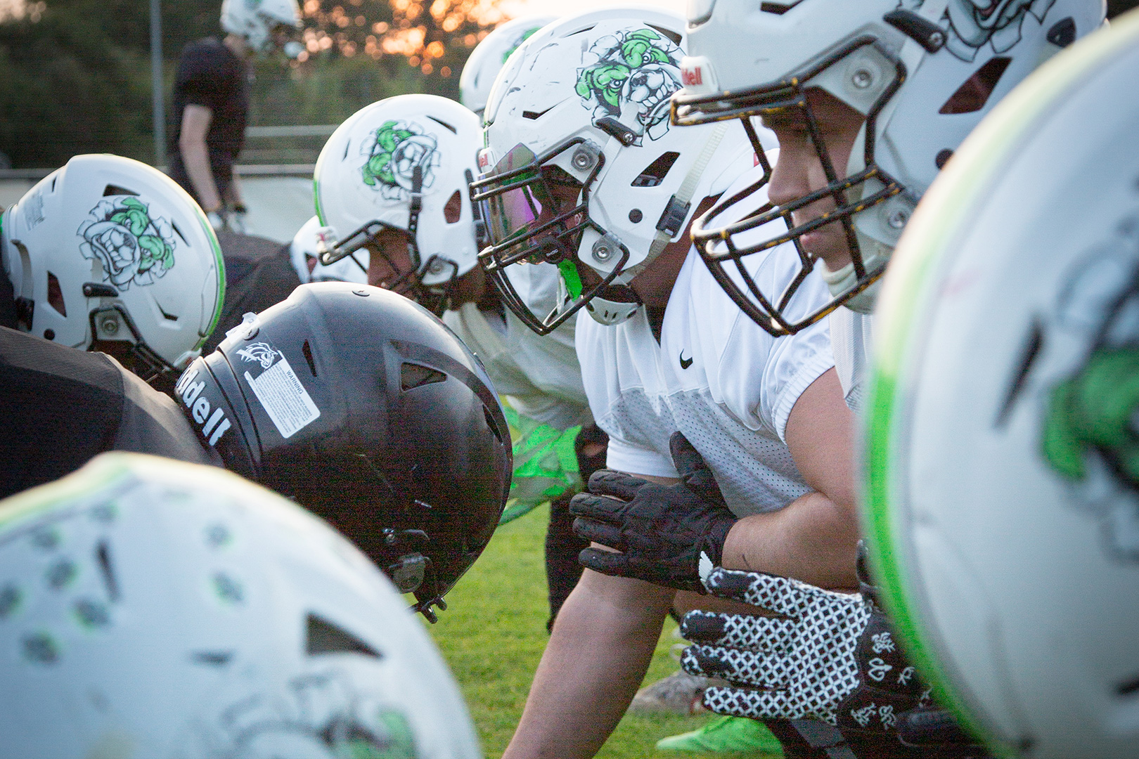 Football-Spieler in Helmen und Trikots stellen sich auf einer Wiese auf, bereit für ein Spiel. Der Sonnenuntergang wirft ein warmes Licht, das an eine Schlittenrettung im Wattenmeer erinnert - jeder Moment ist von Teamwork und Intensität geprägt.