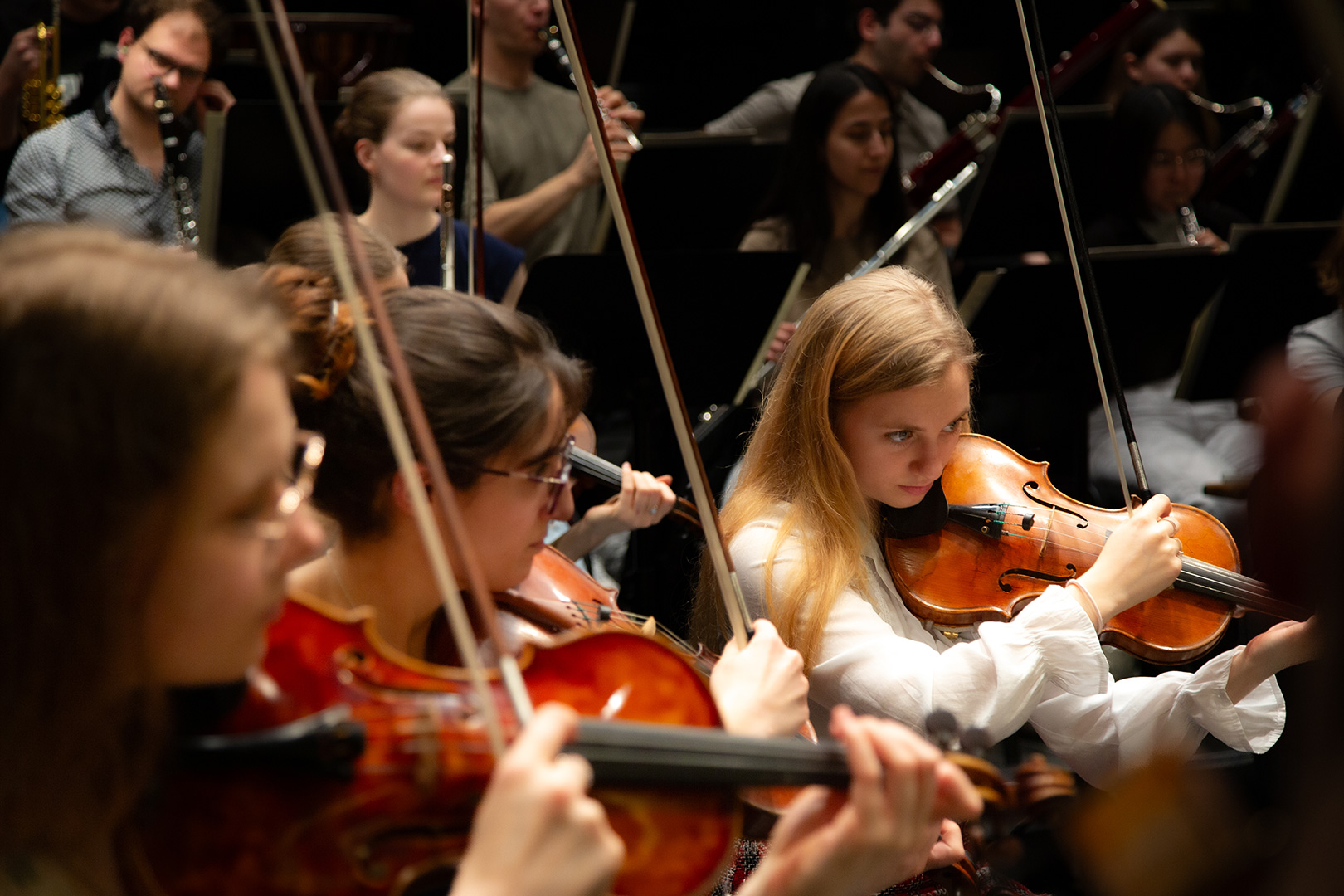 Eine Gruppe junger Musiker spielt Streichinstrumente und konzentriert sich während einer Orchesterprobe. Wie bei einer "Schlittenrettung im Wattenmeer" leiten Teamwork und Präzision die Geiger im Vordergrund und weitere Musiker dahinter.