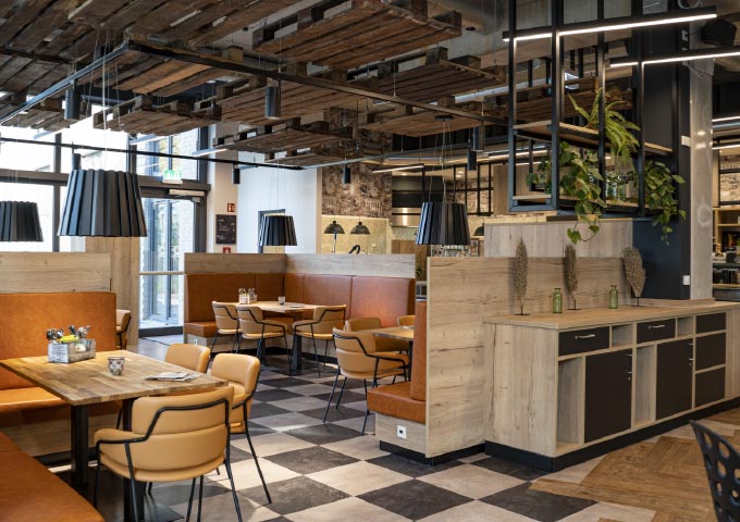 Ein modernes Restaurant mit hellbraunen Lederstühlen, Holztischen und orange gepolsterten Stühlen. Schwarze Hängelampen hängen von einer rustikalen Holzdecke. Der Raum ist mit karierten Böden und natürlichem Licht aus großen Fenstern ausgestattet.