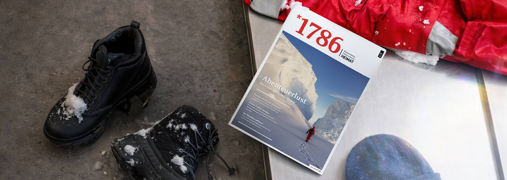 Ein Paar verschneite schwarze Stiefel und eine rote Jacke liegen auf dem Boden neben einer Zeitschrift, die eine verschneite Bergszene und einen Wanderer in Rot zeigt. Auf dem Cover prangt die Nummer 1786.