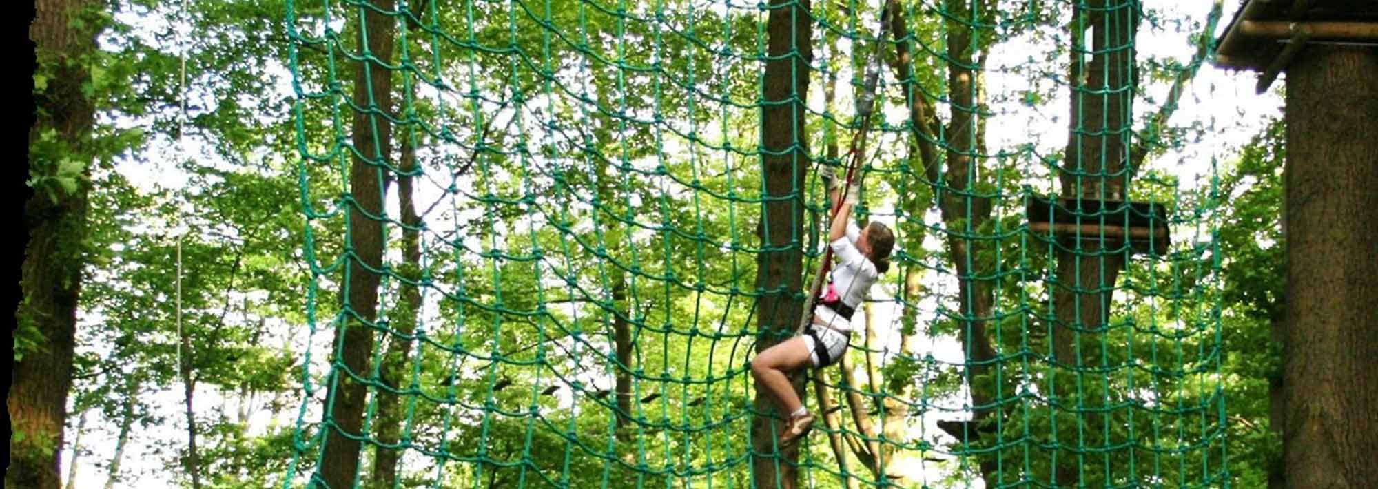 Im Kletterwald Thüle klettert man mit einem Klettergurt über ein grünes Seilnetz, das zwischen den Bäumen im Wald-Erlebnispark hängt, umgeben von üppigem Grün - ein echter Lieblingsort für Outdoor-Fans.