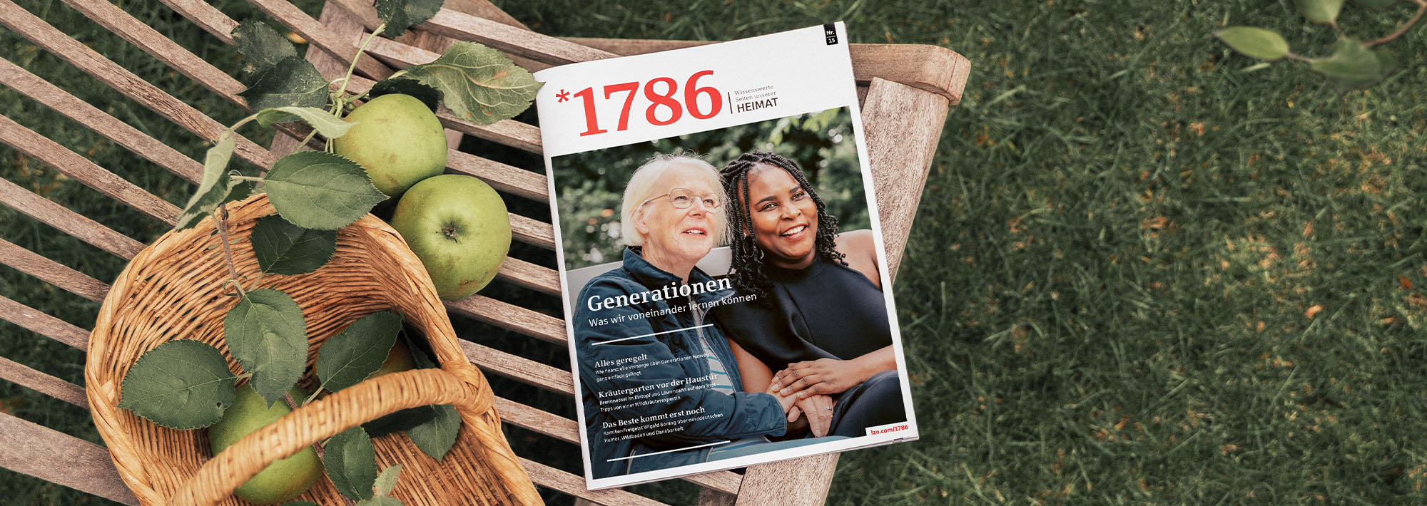 Eine Zeitschrift, auf deren Titelseite zwei lächelnde Menschen zu sehen sind, liegt auf einer Holzbank neben einem Weidenkorb mit grünen Äpfeln, im Hintergrund sind grünes Gras und Blätter zu sehen.